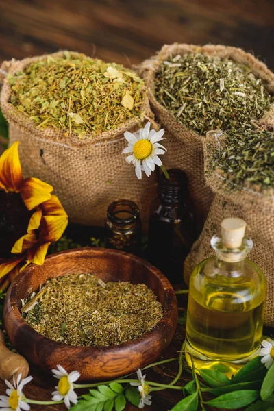 Sackcloth bags with dried herbs, bottles with essential oils and chamomile flowers on wooden surface — Stock Photo