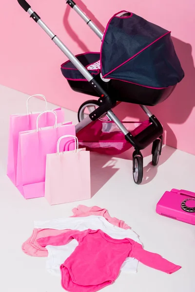 Baby carriage, shopping bags, bodysuits and telephone on pink — Stock Photo