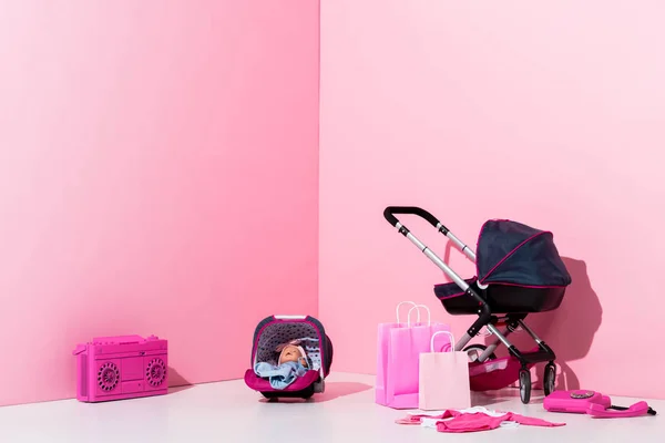 Детская коляска, кукла в детской коляске, сумки и бумбокс на розовый — стоковое фото
