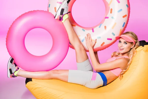 Menina feliz atraente na cadeira do saco do feijão com anéis infláveis do mergulho no rosa, conceito da boneca — Fotografia de Stock