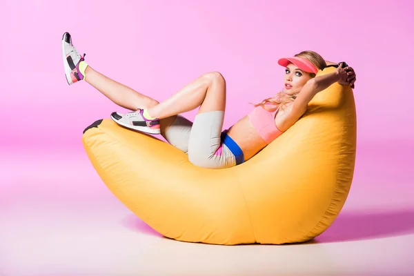 Hermosa chica en sombrero de la visera del sol sentado en la silla de la bolsa de frijol en rosa, concepto de muñeca - foto de stock