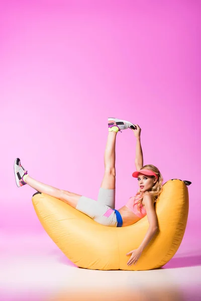 Niña en sombrero de la visera del sol sentado en silla de la bolsa de frijol en rosa, concepto de muñeca - foto de stock