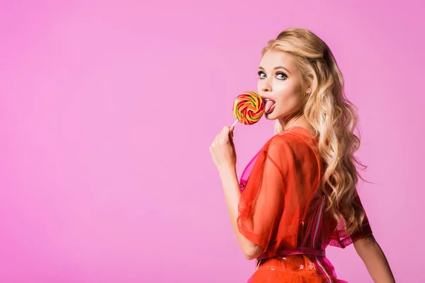 Schönes Mädchen leckt Lutscher isoliert auf rosa, Puppenkonzept — Stockfoto