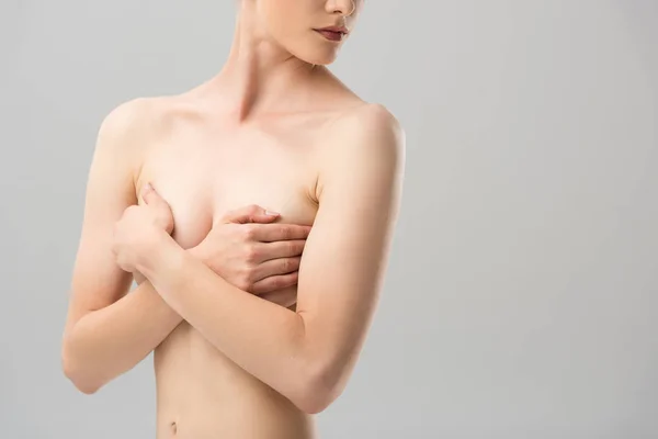 Частичный вид сексуальной обнаженной девушки, покрывающей грудь, изолированной на серой — стоковое фото