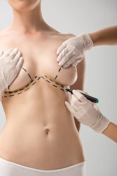 Cropped view of plastic surgeon in latex gloves making marks on breast isolated on grey — Stock Photo