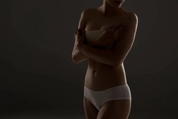 Cropped view of woman in panties with breast bandage in darkness — Stock Photo