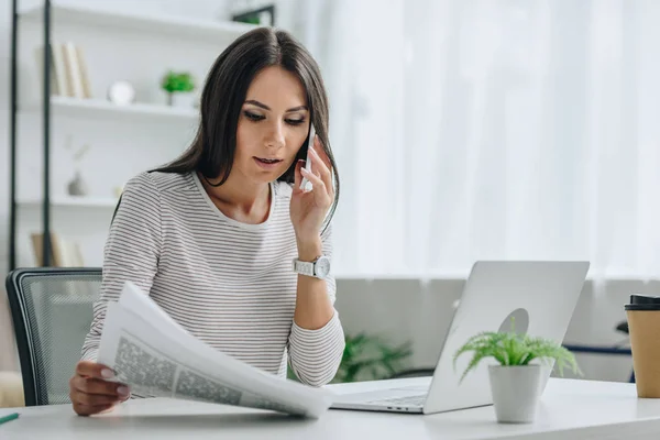 Schöne und brünette Frau, die mit Smartphone spricht und Zeitung hält — Stockfoto