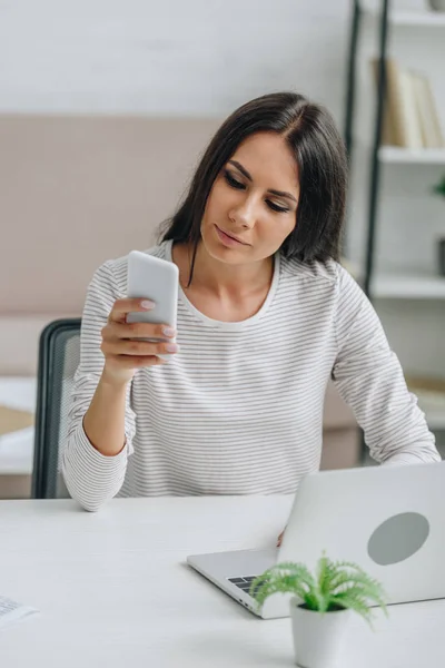 Mulher bonita e morena em jersey usando smartphone no apartamento — Fotografia de Stock