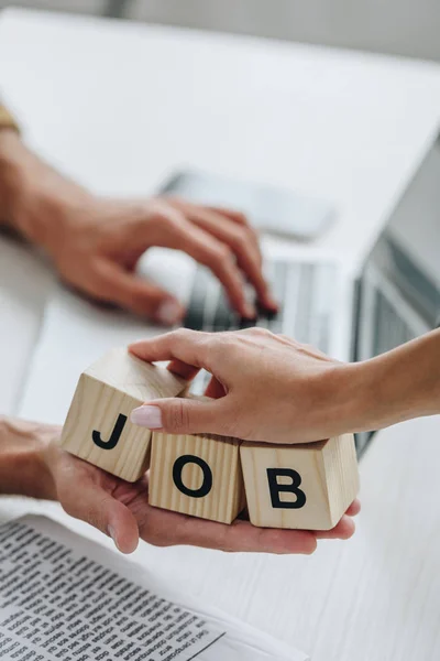 Cropped view of woman and man using laptop and holding cubes with lettering job — Stock Photo