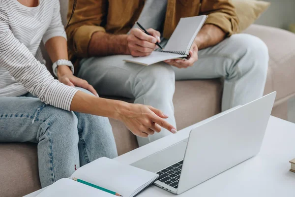 Cropped view of woman pointing with finger at laptop and man writing in notebook — Stock Photo