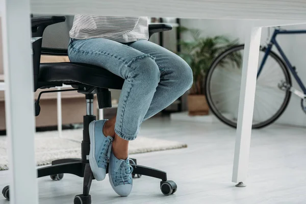 Обрезанный вид женщины в джинсах и кроссовках, сидящей на стуле — стоковое фото