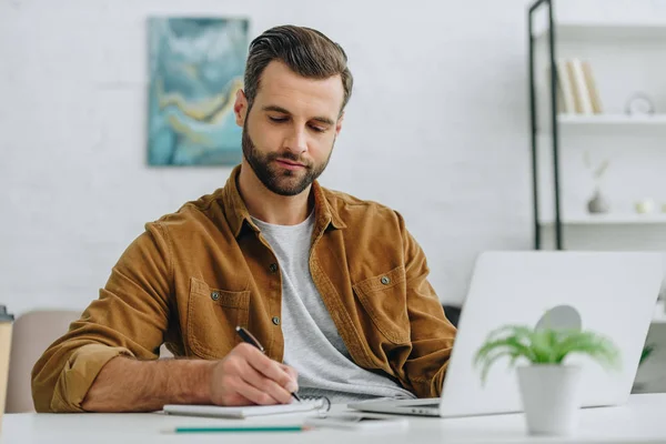 Schöner Mann schreibt in Notizbuch mit Stift in Wohnung — Stockfoto