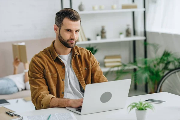 Handsome man using laptop and looking away in apartment — Stock Photo