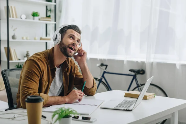 Uomo sorridente e bello che ascolta musica, tiene la matita e alza lo sguardo — Foto stock