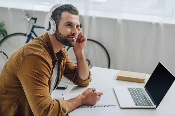 Hombre guapo escuchando música, sosteniendo el lápiz y mirando hacia otro lado - foto de stock