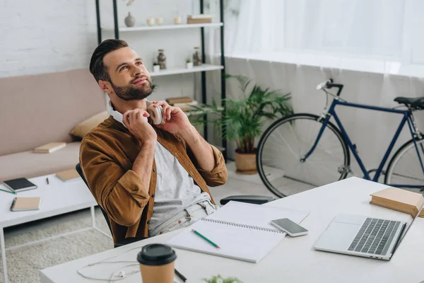 Hombre soñador y guapo sosteniendo los auriculares y mirando hacia arriba - foto de stock