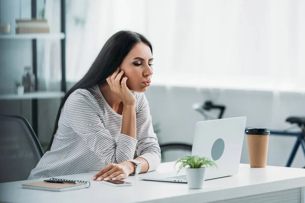 Mulher bonita e morena olhando para a tela do laptop e fazendo rostos — Fotografia de Stock