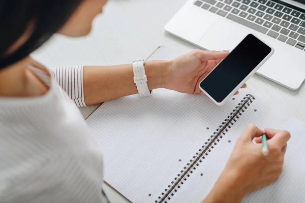 Cropped view of woman writing in notebook and holding smartphone — Stock Photo