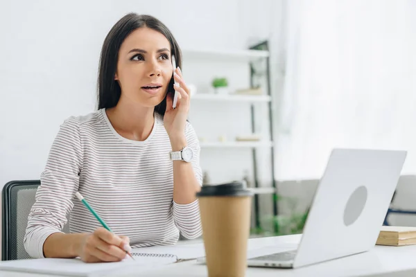 Schöne Frau hält Bleistift in der Hand und spricht mit Smartphone in Wohnung — Stockfoto