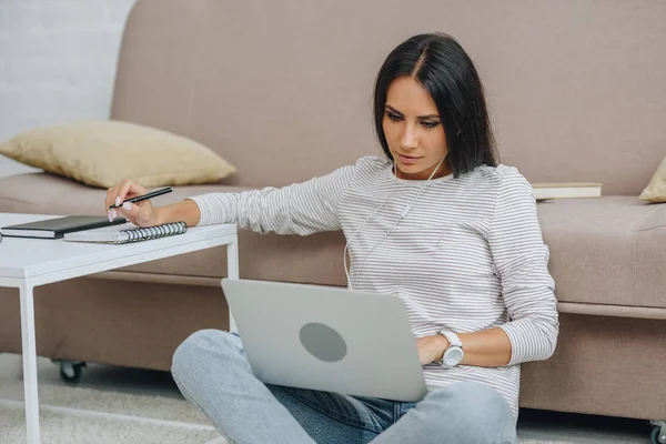 Hermosa mujer con auriculares sentados en el suelo usando el ordenador portátil y la pluma de celebración - foto de stock