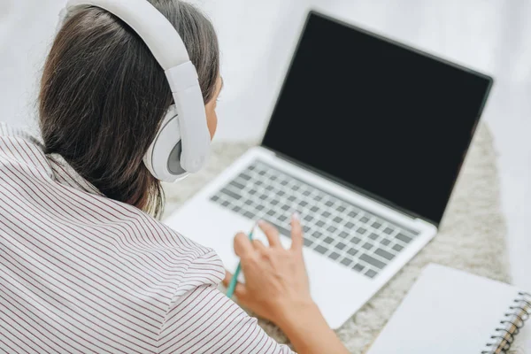 Vista posteriore della donna con cuffie utilizzando il computer portatile e tenendo la matita — Foto stock