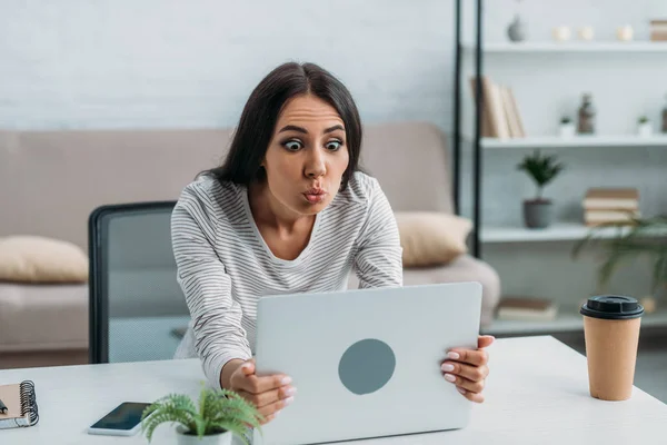 Beautiful and brunette woman looking at screen of laptop and making faces — Stock Photo