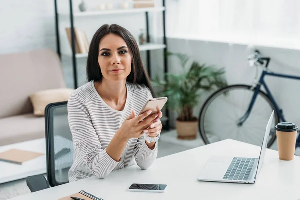 Attractive and shocked woman holding smartphone and looking at camera — Stock Photo