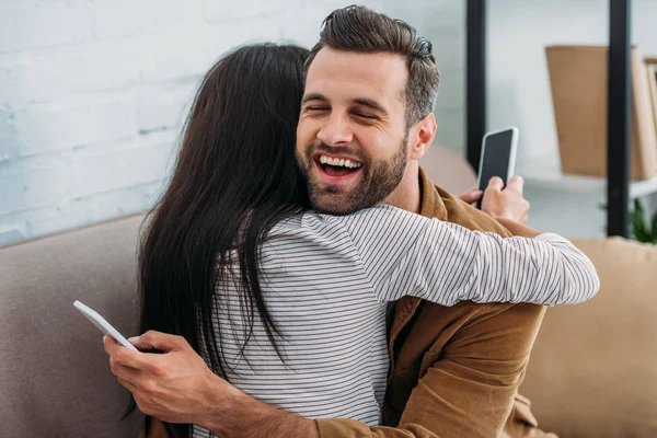 Щасливий і красивий чоловік обіймається з жінкою і тримає смартфон — стокове фото