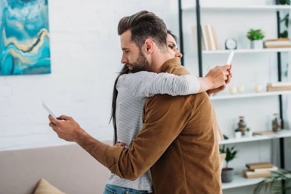 Handsome man hugging with attractive woman and using smartphones — Stock Photo