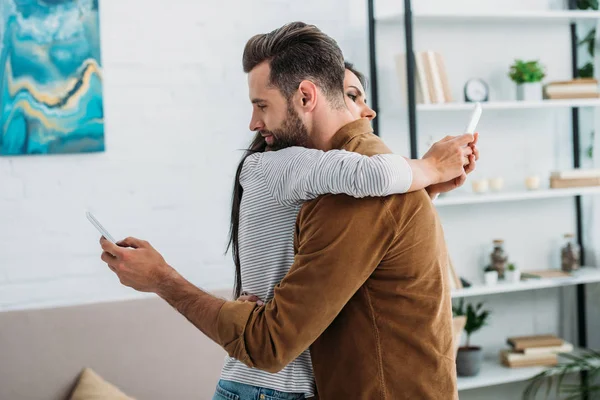 Hombre guapo abrazo con mujer atractiva y el uso de teléfonos inteligentes - foto de stock