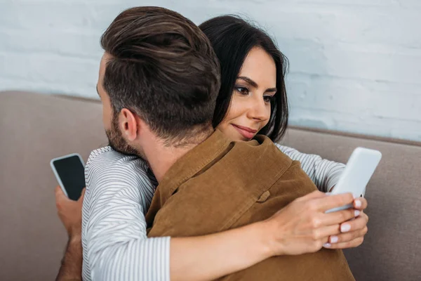 Man and attractive, brunette woman hugging and using smartphones — Stock Photo