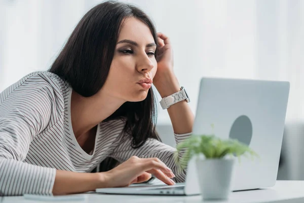 Selective focus of beautiful and brunette woman using laptop and making faces — Stock Photo