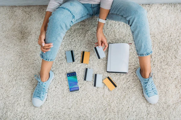 Partial view of  woman sitting on floor with notebook, smartphone and holding credit card — Stock Photo