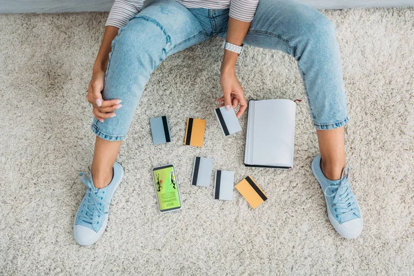 Vista superior de la mujer en jeans con tarjetas de crédito cerca de teléfono inteligente con aplicación de compras - foto de stock