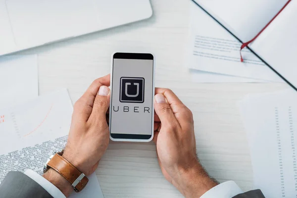 Vista superior del hombre sosteniendo teléfono inteligente con uber sitio web - foto de stock