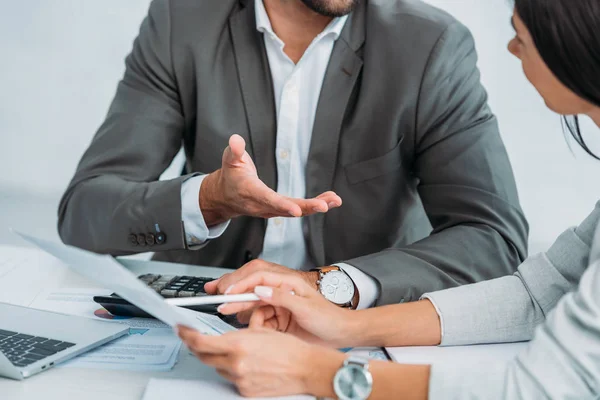 Cropped view of businessman and businesswoman woman in suits discussing document — Stock Photo