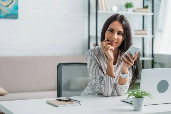 Attractive and brunette woman holding smartphone and looking away — Stock Photo