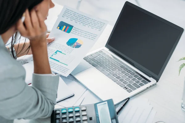 Vista ritagliata della donna in possesso di carta e guardando lo schermo del computer portatile — Foto stock