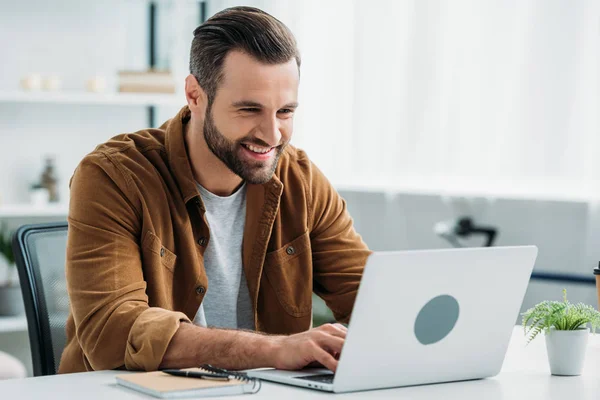 Hombre guapo y feliz sonriendo y mirando la pantalla de la computadora portátil — Stock Photo