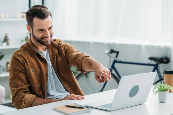 Schöner und glücklicher Mann, der lächelt und mit dem Finger auf den Bildschirm seines Laptops zeigt — Stockfoto