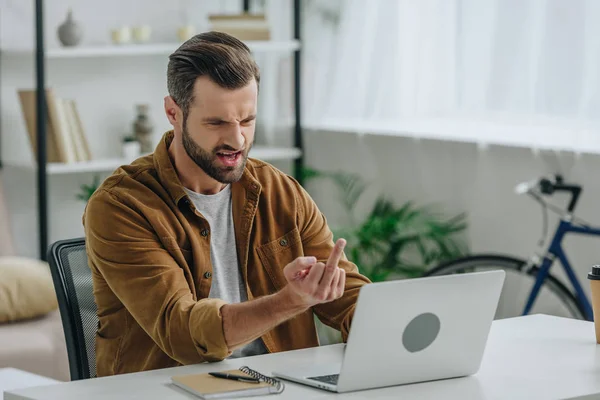 Hombre guapo y agresivo mostrando el dedo medio en la pantalla de la computadora portátil - foto de stock