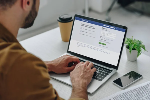 Vista cortada do homem usando laptop com site facebook na tela — Fotografia de Stock