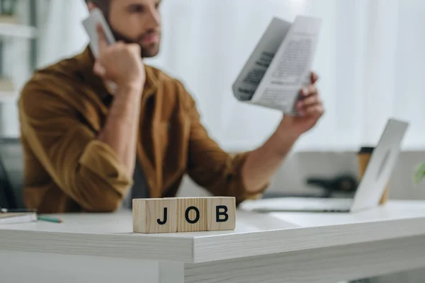 Enfoque selectivo de cubos de madera con trabajo de letras y el hombre hablando en el teléfono inteligente en el fondo - foto de stock