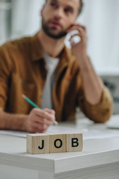 Selective focus of wooden cubes with lettering job and man talking on smartphone on background — Stock Photo