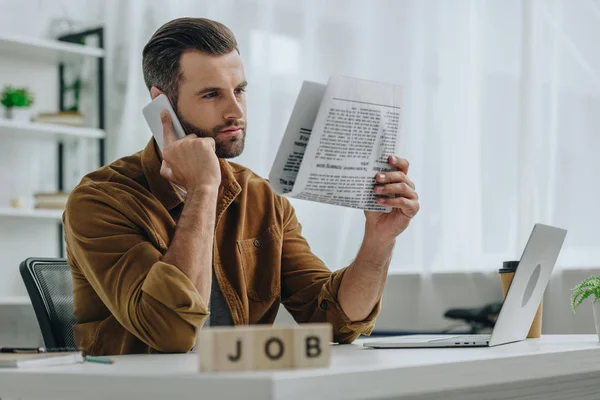 Enfoque selectivo de cubos de madera con trabajo de letras y el hombre hablando en el teléfono inteligente y la celebración de periódico - foto de stock