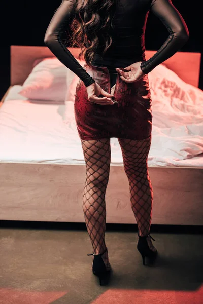 Vista ritagliata della prostituta spogliarsi in camera da letto con luci rosse su nero — Foto stock