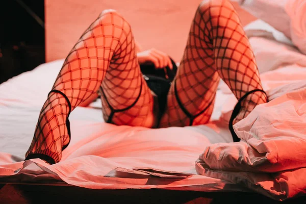 Selektiver Fokus der Prostituierten in Strümpfen, die auf weißer Bettwäsche in der Nähe von Dollarnoten liegen — Stockfoto