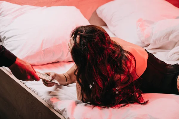 Обрезанный вид человека, дающего деньги проститутке в корсете на кровати — стоковое фото