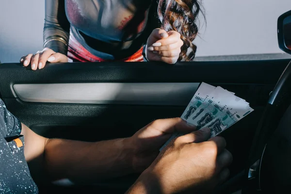 Vista ritagliato di uomo in auto in possesso di denaro contante vicino prostituta — Stock Photo