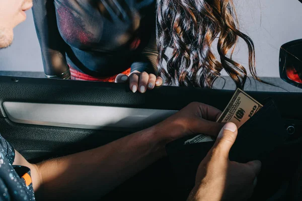 Обрезанный вид человека в машине, держащего бумажник с наличными возле проститутки — стоковое фото